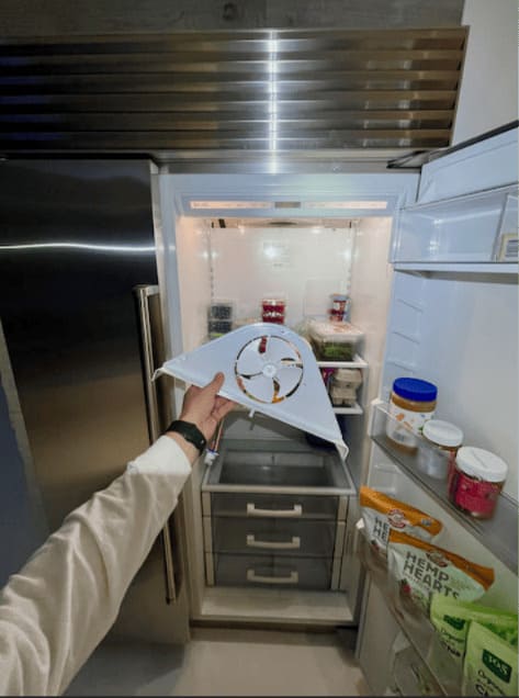 Certified Sub-Zero technician holding a genuine OEM evaporator fan housing during a preventive maintenance tune-up in a South Tampa kitchen